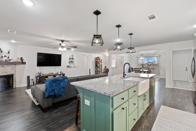 kitchen with decorative light fixtures, sink, a kitchen island with sink, green cabinetry, and light stone countertops