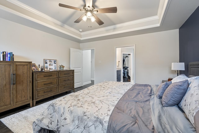 bedroom featuring dark wood-type flooring, ceiling fan, ornamental molding, and a tray ceiling