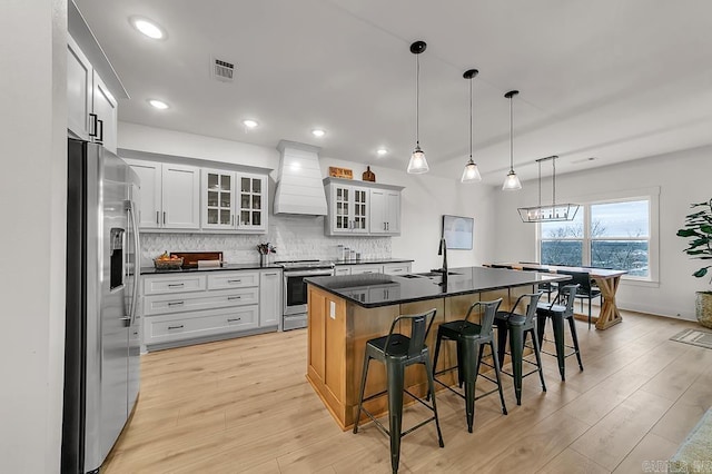 kitchen with sink, a kitchen breakfast bar, stainless steel appliances, custom range hood, and a center island with sink