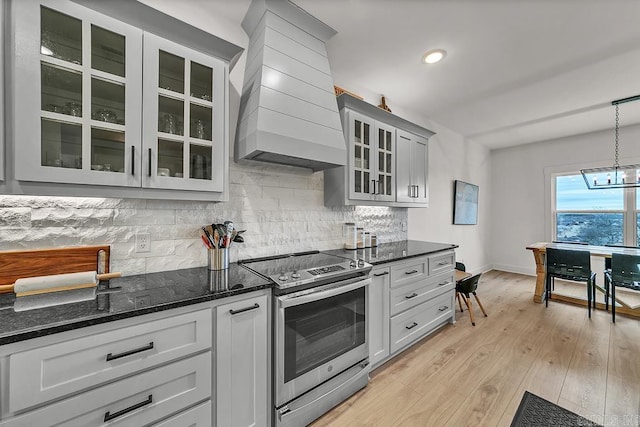 kitchen featuring stainless steel electric range oven, premium range hood, pendant lighting, tasteful backsplash, and light hardwood / wood-style flooring