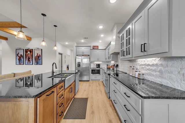 kitchen with tasteful backsplash, light hardwood / wood-style flooring, hanging light fixtures, dark stone countertops, and appliances with stainless steel finishes