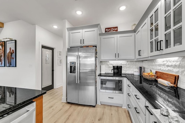 kitchen with appliances with stainless steel finishes, tasteful backsplash, white cabinets, dark stone counters, and light wood-type flooring