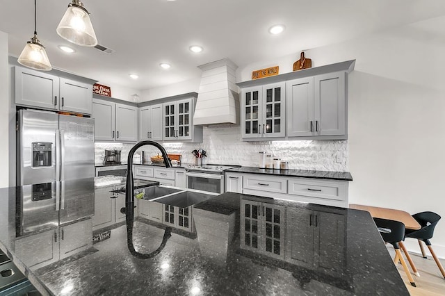 kitchen featuring backsplash, dark stone counters, custom exhaust hood, hanging light fixtures, and stainless steel appliances