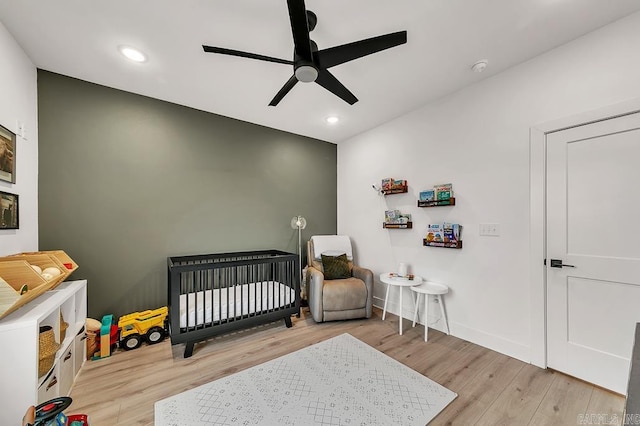 bedroom with a nursery area, ceiling fan, and light wood-type flooring