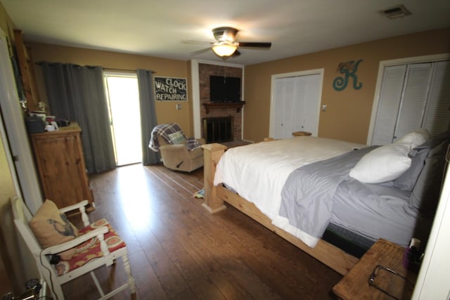 bedroom with multiple closets, ceiling fan, wood-type flooring, and a brick fireplace