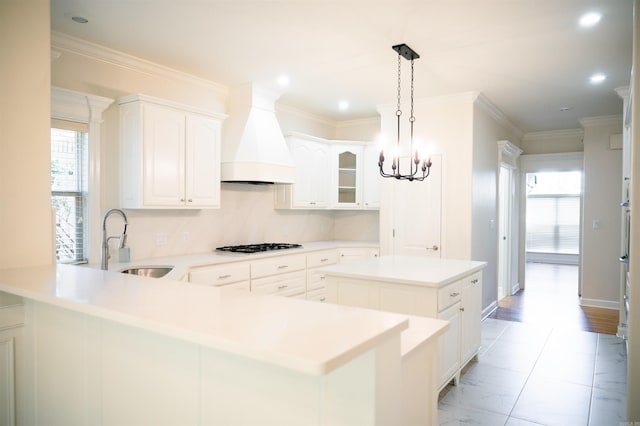 kitchen with premium range hood, white cabinetry, sink, a center island, and crown molding