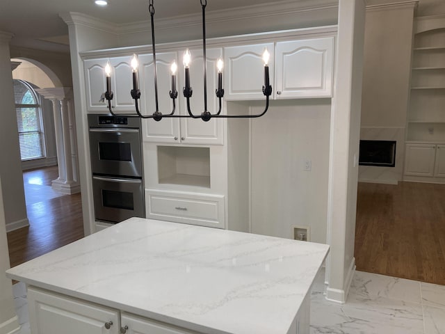 kitchen with stainless steel double oven, decorative light fixtures, light stone countertops, and white cabinets