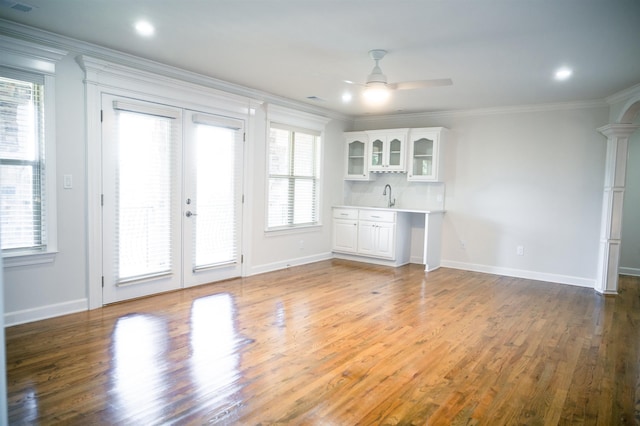 interior space with ornate columns, indoor wet bar, ornamental molding, hardwood / wood-style flooring, and ceiling fan