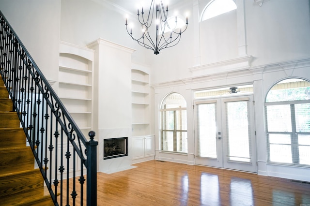 living room with built in features, hardwood / wood-style floors, a towering ceiling, a high end fireplace, and french doors