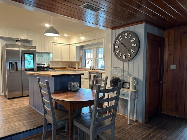 kitchen featuring wooden counters, appliances with stainless steel finishes, white cabinets, a kitchen island, and decorative light fixtures