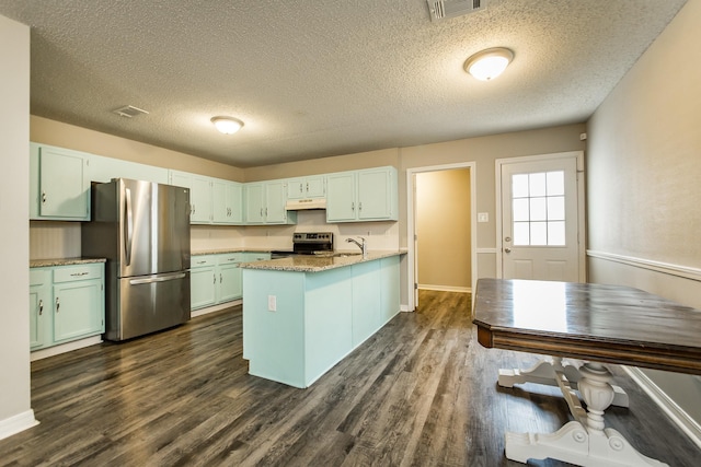 kitchen with appliances with stainless steel finishes, a kitchen island with sink, a textured ceiling, and dark hardwood / wood-style flooring