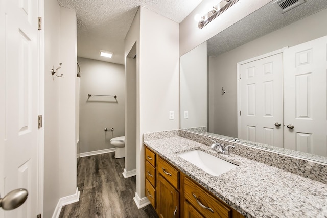 bathroom featuring vanity, wood-type flooring, toilet, and a textured ceiling