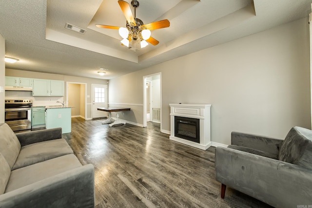 living room with dark wood-type flooring, ceiling fan, a raised ceiling, and a textured ceiling