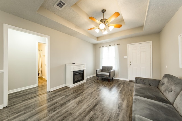 unfurnished living room featuring ceiling fan, dark hardwood / wood-style floors, a raised ceiling, and a textured ceiling