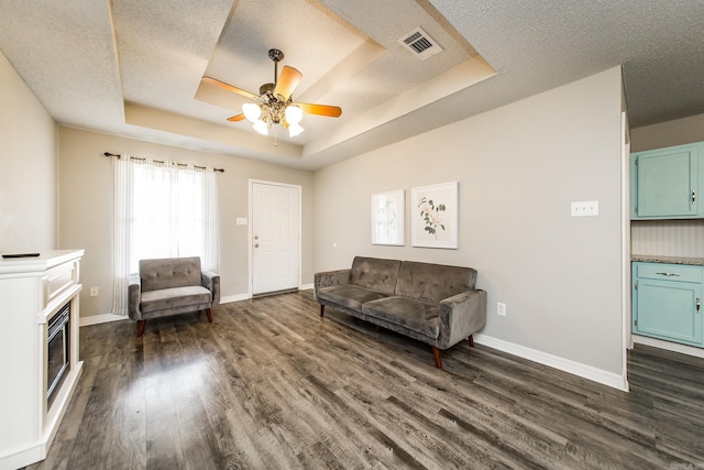 living room with dark hardwood / wood-style flooring, ceiling fan, a tray ceiling, and a textured ceiling