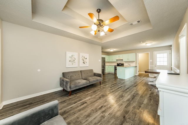 living room with dark wood-type flooring, a textured ceiling, ceiling fan, and a tray ceiling