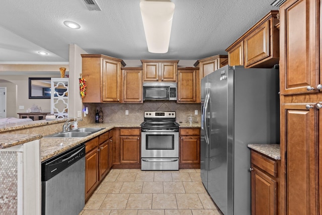 kitchen with sink, decorative backsplash, stainless steel appliances, and light stone countertops