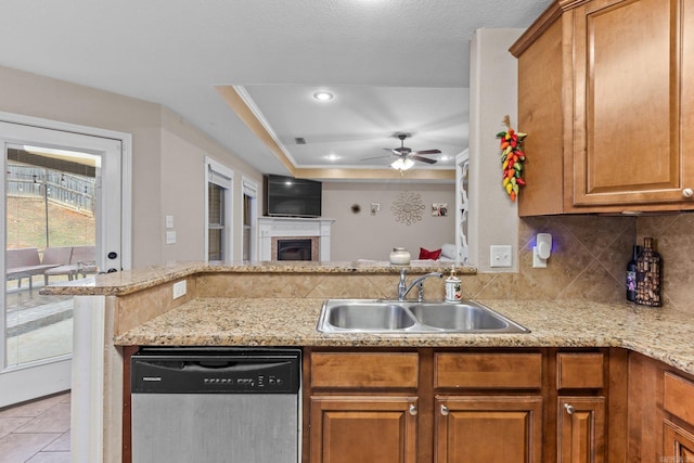 kitchen featuring sink, light stone counters, stainless steel dishwasher, a raised ceiling, and backsplash