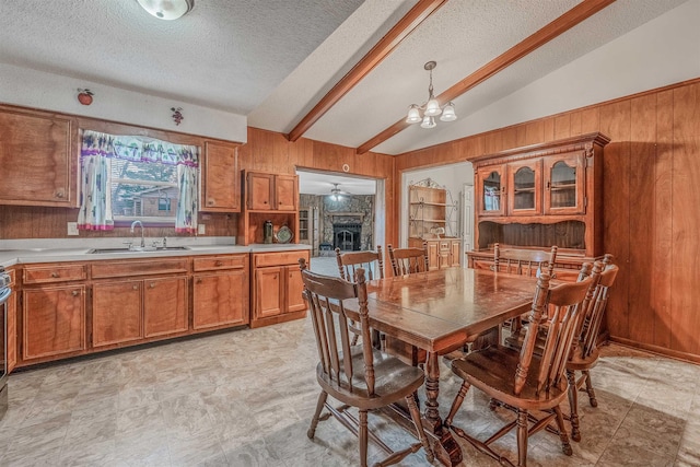 dining room with sink, an inviting chandelier, lofted ceiling with beams, wooden walls, and a fireplace