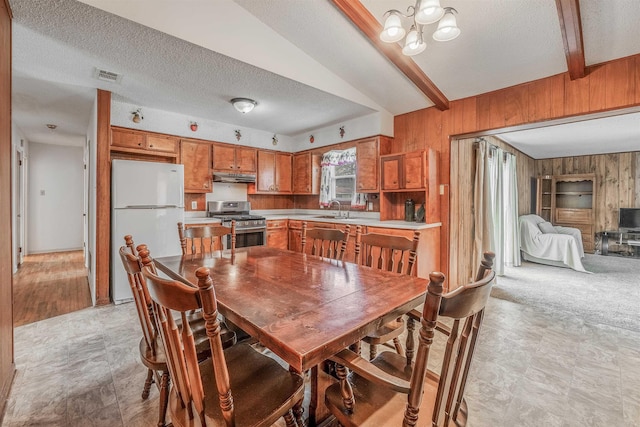 dining room featuring sink, beam ceiling, wooden walls, and a textured ceiling