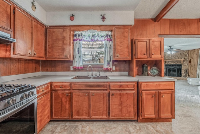 kitchen with a stone fireplace, wooden walls, sink, stainless steel gas range, and a textured ceiling