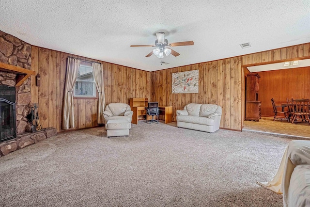 carpeted living room featuring ceiling fan, a fireplace, a textured ceiling, and wood walls