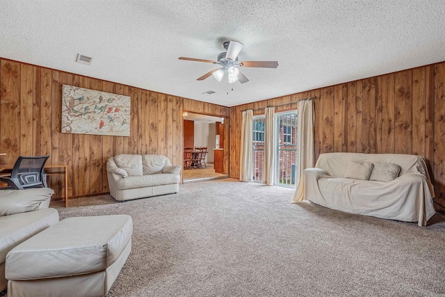 carpeted living room featuring ceiling fan, wooden walls, and a textured ceiling