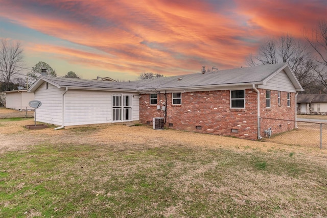 back house at dusk featuring a lawn and central air condition unit