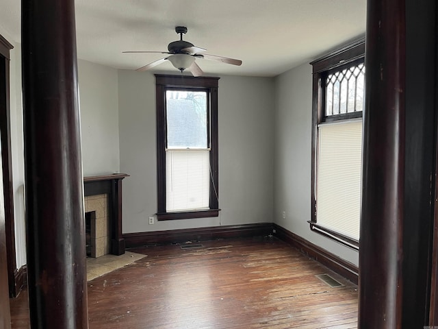 unfurnished living room with wood-type flooring, a wealth of natural light, a fireplace, and ceiling fan