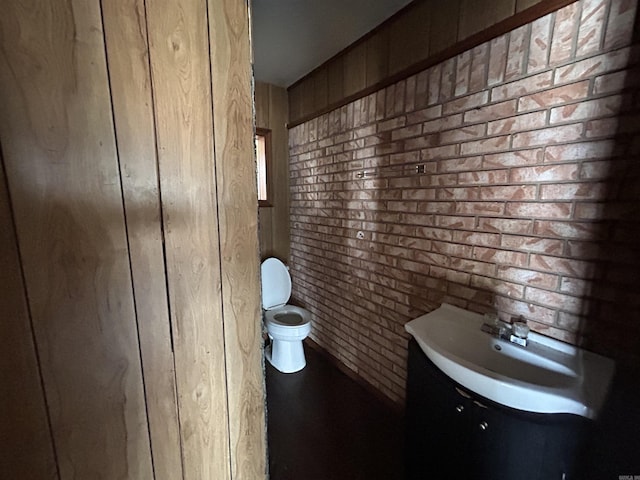 bathroom with brick wall, toilet, and vanity