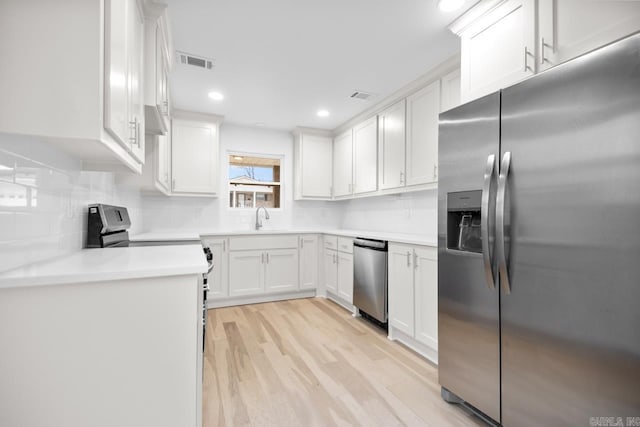 kitchen featuring white cabinetry, sink, backsplash, stainless steel appliances, and light hardwood / wood-style flooring