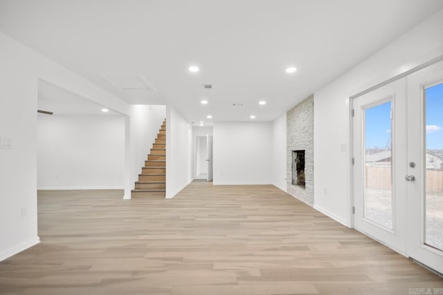 unfurnished living room featuring french doors, a large fireplace, and light hardwood / wood-style floors