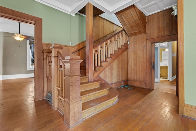 stairs featuring hardwood / wood-style flooring, ornamental molding, ceiling fan, and wood walls