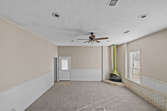 unfurnished living room featuring a wood stove, light colored carpet, a textured ceiling, and ceiling fan