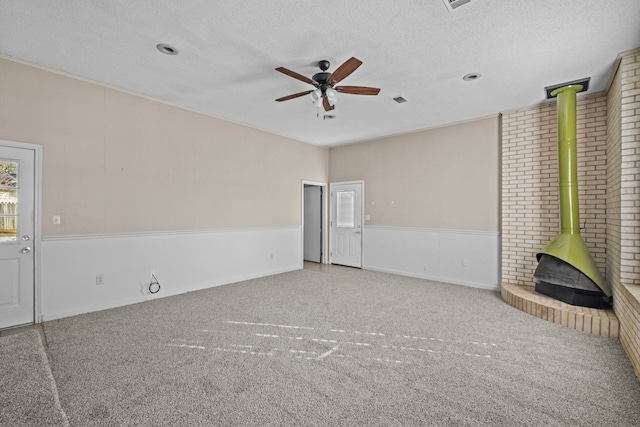 unfurnished living room with carpet flooring, a textured ceiling, ceiling fan, and a wood stove