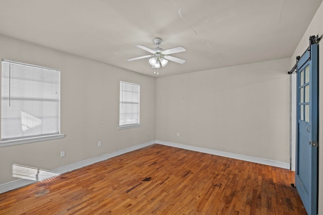 spare room with a barn door, dark hardwood / wood-style floors, and ceiling fan