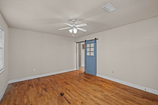 empty room featuring light hardwood / wood-style flooring, a barn door, and ceiling fan