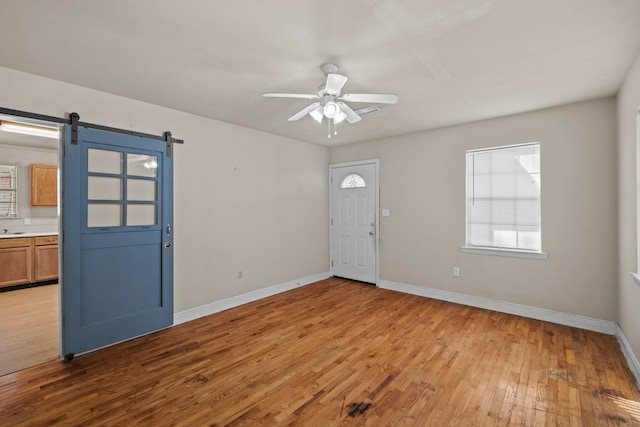 foyer with ceiling fan, a barn door, and light wood-type flooring