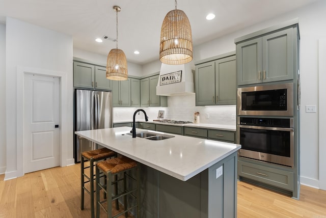 kitchen with sink, decorative light fixtures, appliances with stainless steel finishes, an island with sink, and light hardwood / wood-style floors