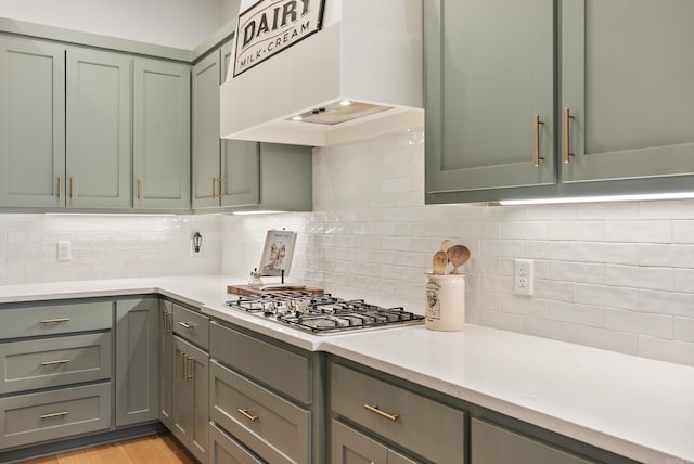 kitchen with decorative backsplash, light hardwood / wood-style flooring, stainless steel gas cooktop, and premium range hood