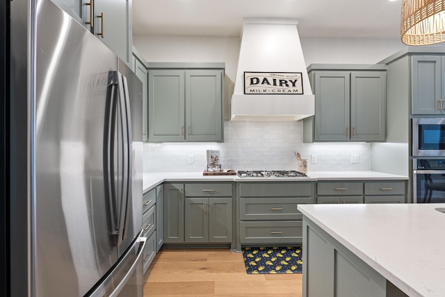 kitchen featuring light hardwood / wood-style flooring, stainless steel appliances, tasteful backsplash, light stone countertops, and custom range hood