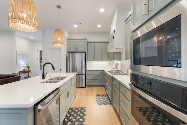 kitchen with premium range hood, sink, hanging light fixtures, stainless steel appliances, and a center island with sink