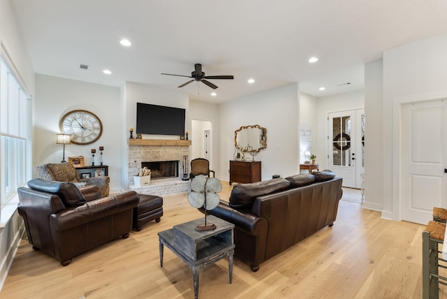 living room featuring a fireplace, ceiling fan, and light wood-type flooring