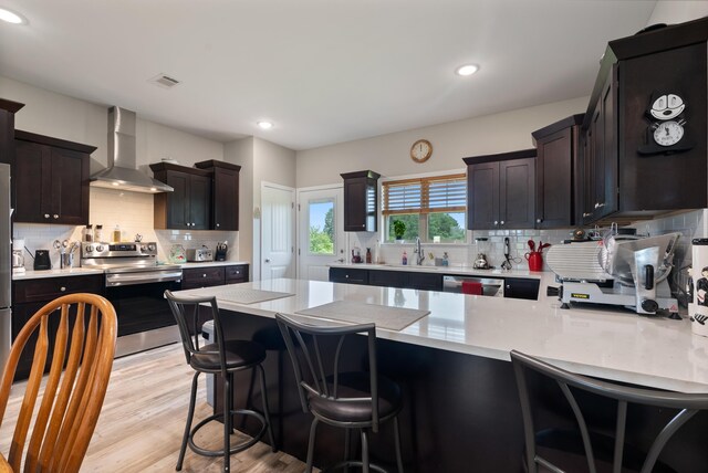 kitchen featuring appliances with stainless steel finishes, sink, a kitchen breakfast bar, wall chimney range hood, and light hardwood / wood-style flooring