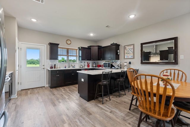 kitchen with a breakfast bar, light hardwood / wood-style flooring, decorative backsplash, kitchen peninsula, and wall chimney exhaust hood