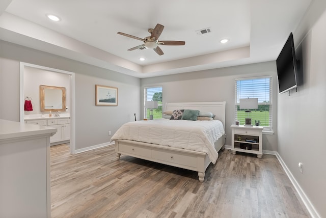 bedroom with sink, ensuite bath, light hardwood / wood-style floors, and a raised ceiling