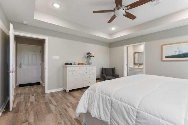 bedroom with connected bathroom, a tray ceiling, light hardwood / wood-style floors, and ceiling fan