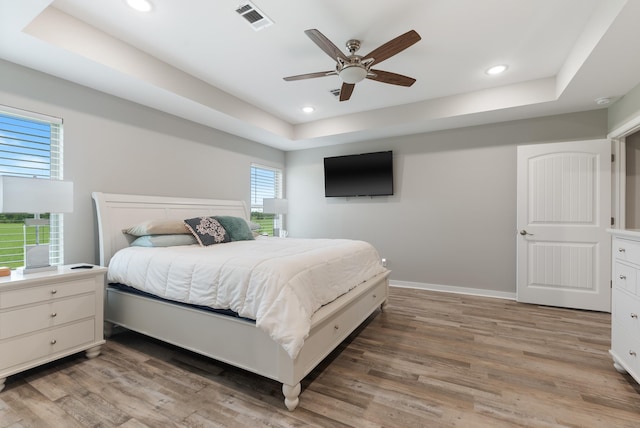 bedroom featuring ceiling fan, wood-type flooring, and a raised ceiling