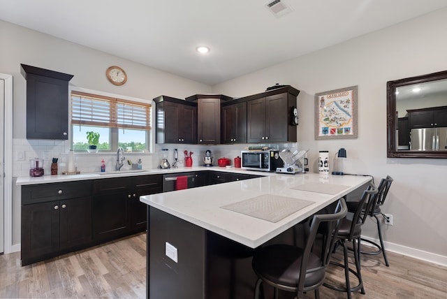 kitchen with a kitchen bar, sink, kitchen peninsula, stainless steel appliances, and backsplash