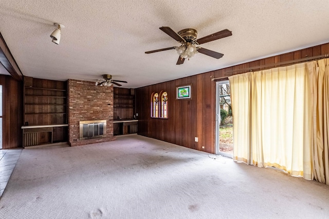 unfurnished living room with light colored carpet, wooden walls, a brick fireplace, and a textured ceiling